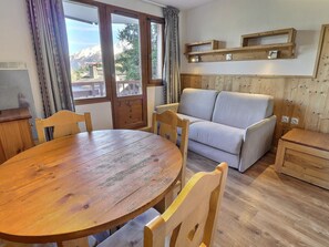 A cozy room with a wooden dining table, two chairs, a sofa, and a small wooden cabinet.