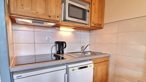 A compact kitchen with wooden cabinets, a microwave, a coffee maker, a sink, and a dishwasher. - Comfortable 2 Rooms, Ski-In/Ski-Out, Close to Shops (La Tania)