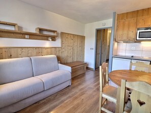 Ein gemütlicher Wohnbereich mit einer Couch, Holzboden und einem Esstisch mit Stühlen.