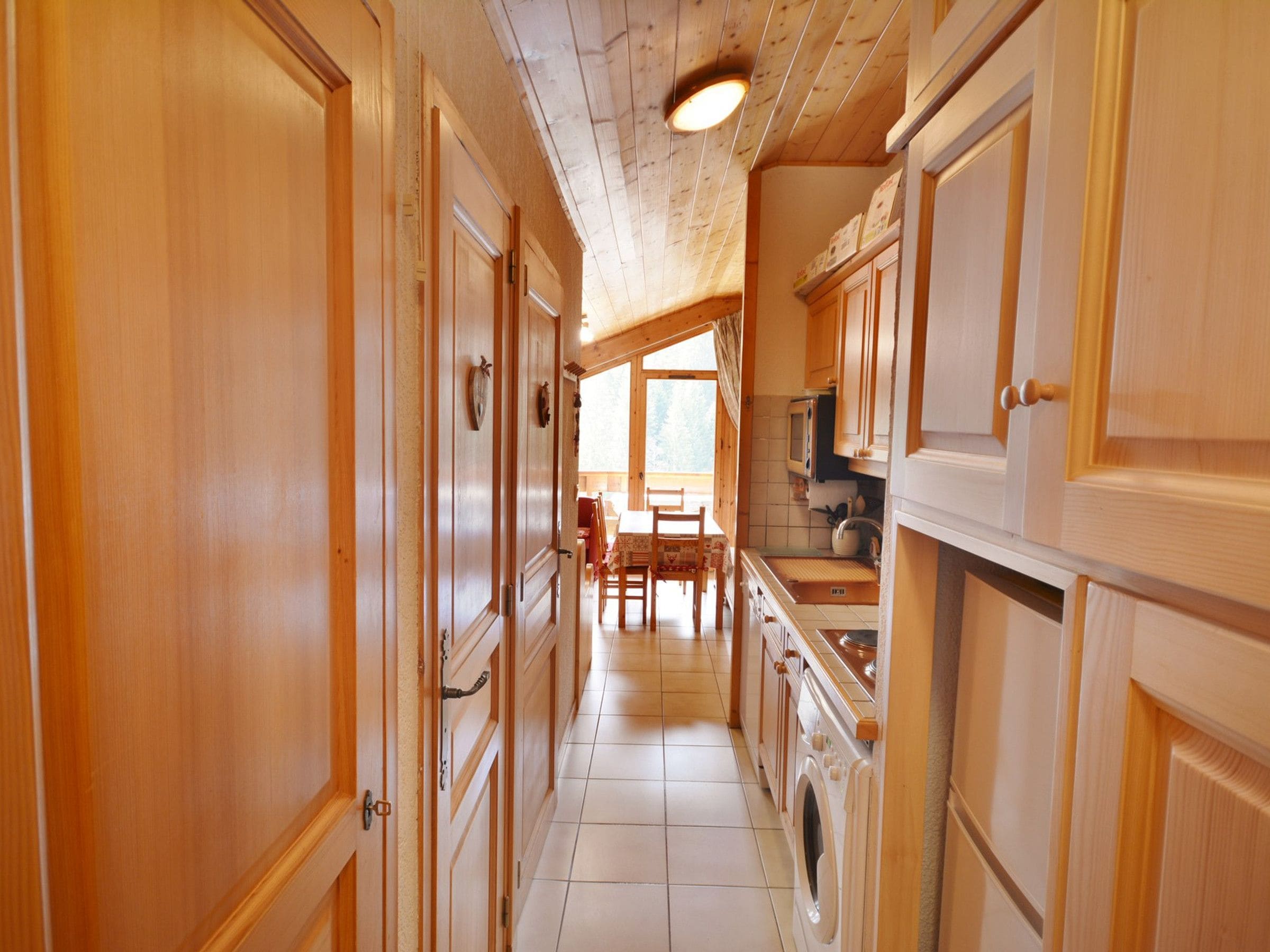 A narrow hallway with wooden doors and cabinets, leading to a dining area with a table and chairs.
