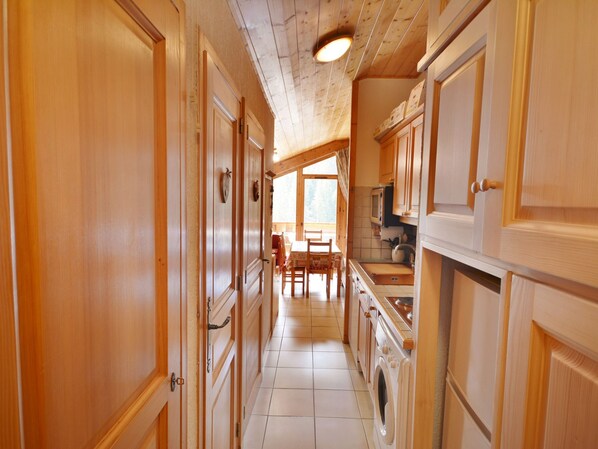 A narrow hallway with wooden doors and cabinets, leading to a dining area with a table and chairs.