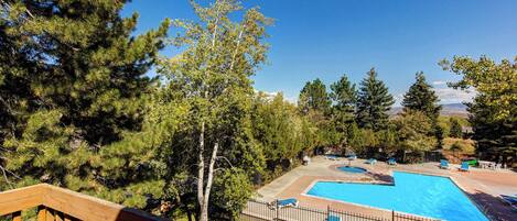 A pool with lounge chairs, surrounded by trees and a wooden deck.