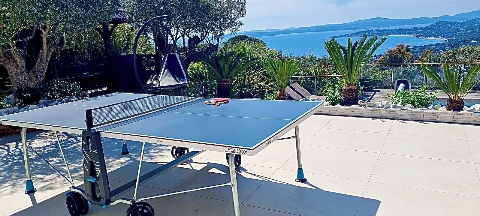 A ping pong table set up outdoors with a scenic view of the sea and mountains in the background.