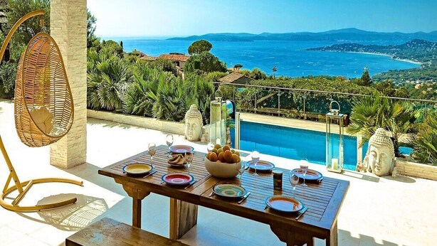 Ein Esstisch, gedeckt mit Tellern, Gläsern und einer Schüssel Brot, mit Blick auf einen Pool und eine schöne Aussicht auf Meer und Hügel.