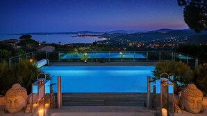 Ein Schwimmbad mit Blick auf das Meer und ferne Stadtlichter bei Nacht.
