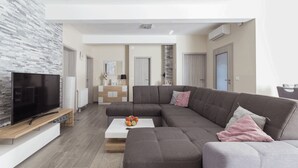 A modern living room with a sectional sofa, a flat-screen TV, a coffee table with fruit, and a stone accent wall. - Villa Nicolle (Privlaka)