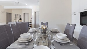 A dining area with a table set for four, surrounded by grey upholstered chairs. - Villa Nicolle (Privlaka)