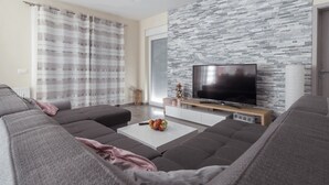 A modern living room with a sectional sofa, a flat-screen TV, and a stone-textured wall. - Villa Nicolle (Privlaka)