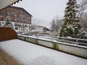 A snowy outdoor area with a building, a wooden fence, and a metal railing.