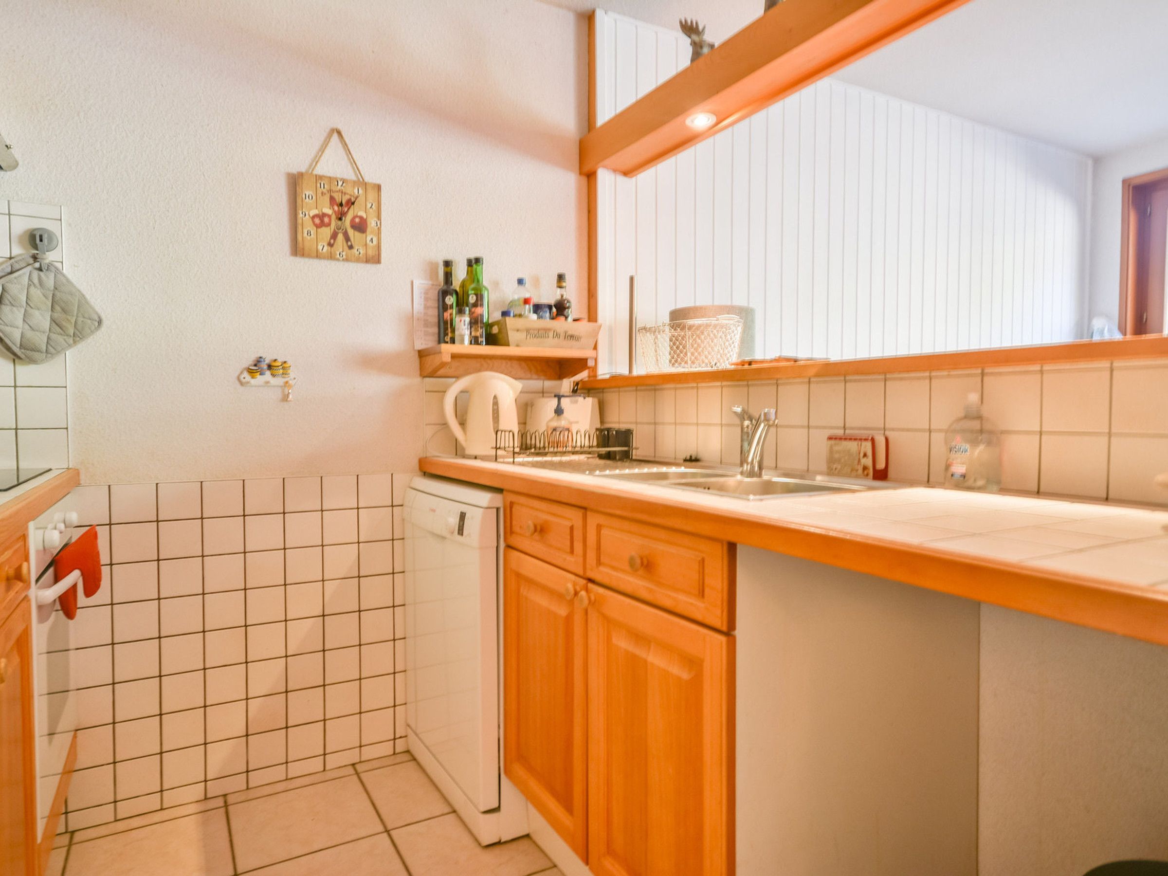 A compact kitchen with a dishwasher, wooden cabinets, a sink, and a hanging clock.