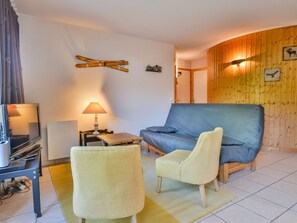 A cozy room with a sofa, two armchairs, a lamp, a television, and a wooden wall with wall art. - Apartment Morzine 6 pers, near slopes, terrace, parking (Morzine)