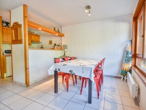 A dining area with a table set for four, surrounded by red chairs, in a room with white walls and a kitchen area to the left. - Apartment Morzine 6 pers, near slopes, terrace, parking (Morzine)