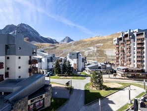 A modern hotel with multiple floors, a parking area, and a view of mountains in the background.