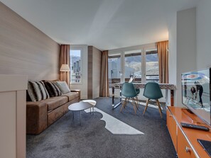 A modern hotel room with a sofa, two chairs, a small table, and a TV.