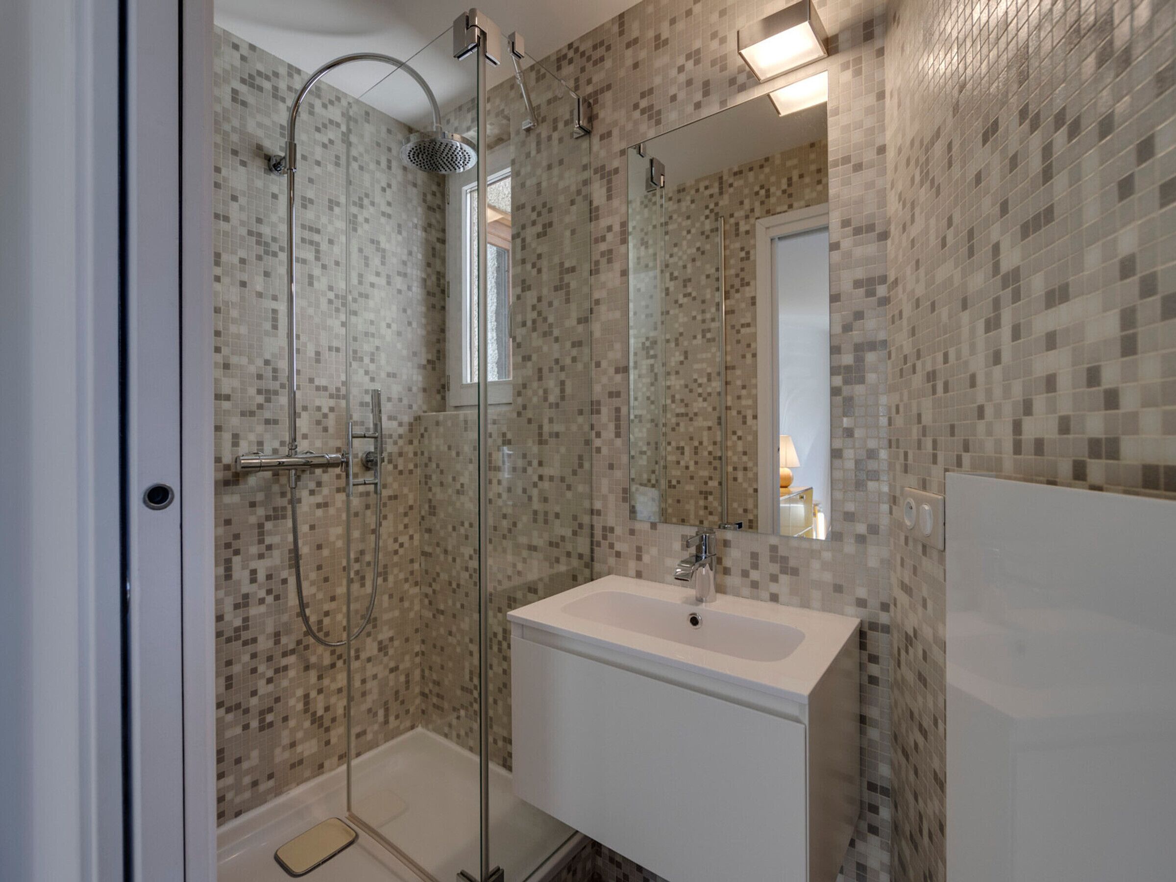 Une salle de bain moderne avec une douche à parois de verre, un lavabo blanc et des murs recouverts de mosaïques.