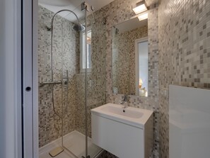 A modern bathroom with a glass-enclosed shower, a white sink, and mosaic tile walls.