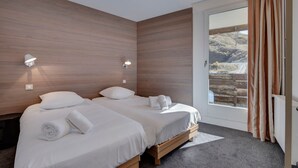 A room with two beds, wooden walls, and a large window with curtains.