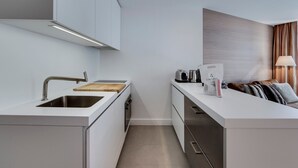 A modern kitchen with a sink, stove, and countertop. There is a small island with a cutting board and a bag of groceries. The room has a wooden accent wall and a lamp.