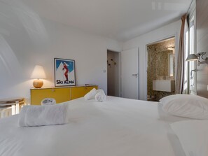 A hotel room with a bed, a yellow dresser, a poster, a lamp, and a bathroom visible through an open door.