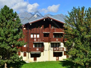 Ein mehrstöckiges Chalet mit Balkonen vor einer Bergkulisse.