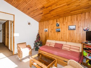 A cozy living room with a wooden ceiling, a sofa, a coffee table, and a Christmas tree.