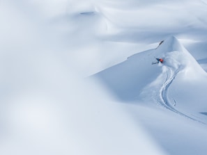 A snowy mountain landscape with a skier carving a path in the snow.