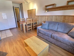A living room with a wooden floor, a grey sofa, a wooden coffee table, and a dining area with wooden chairs and a table.