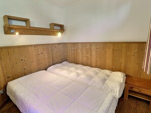A wooden-framed bed with a quilted white duvet, a wooden headboard, and a small shelf with a light fixture above it.