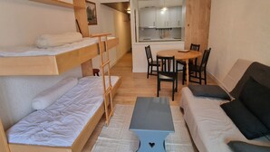 Ein kleines Zimmer mit Stockbetten, einer Schlafcouch, einem kleinen Tisch und einer Küchenzeile.
