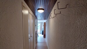 Ein schmaler Korridor mit Holzdielen und weißen Wänden. Auf der linken Seite befinden sich Türen und eine Leuchte an der Decke.