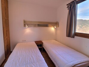 A room with two single beds, a wooden headboard, a nightstand, a window with curtains, and a view of a landscape. - Comfortable 2-room apartment, ski-in/ski-out, sleeps 4 (La Tania)