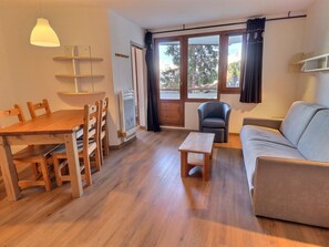 A living room with a wooden dining table, chairs, a sofa, a small wooden table, and a grey armchair. - Comfortable 2-room apartment, ski-in/ski-out, sleeps 4 (La Tania)