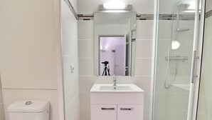 Un baño con inodoro, lavabo con espejo y ducha.