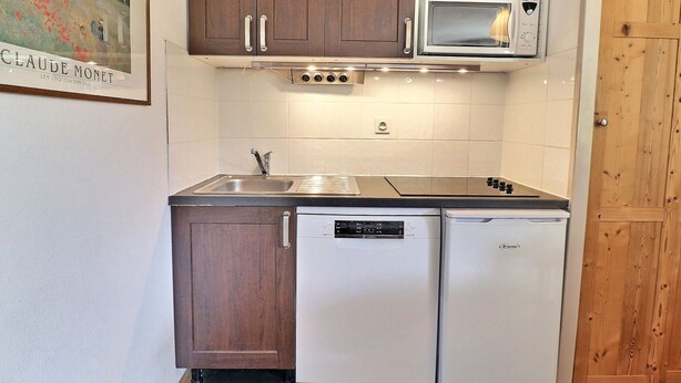 Una cocina compacta con armarios de madera, un lavamanos de acero inoxidable, un microondas y un lavavajillas.