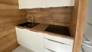Een kleine keuken met een houten spatwand, een zwarte spoelbak en witte kastjes.