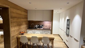 Een moderne keuken met houten details, een eethoek met een houten tafel en stoelen, en inbouwapparatuur.
