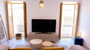 A living room with a TV, two round tables, a sofa with cushions, and a hanging light fixture. - Duplex Penthouse with Jacuzzi in Historic Estepona, near Beach & Attractions (Estepona)