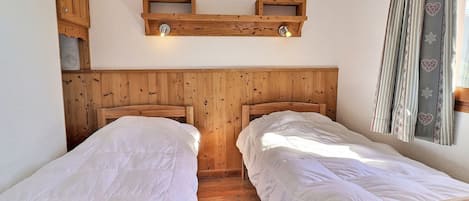 A room with two wooden beds, a wooden headboard, and a shelf with lights.