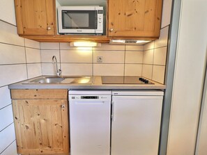 A compact kitchen with wooden cabinets, a built-in microwave, a sink, a stove, and a dishwasher.
