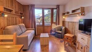 A wooden-furnished living room with a sofa, armchair, coffee table, TV, and wooden cabinets. - Comfortable 2-Room, Ski-in/Ski-out, Close to Shops (La Tania)