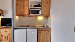 A compact kitchen with wooden cabinets, a microwave, a dishwasher, and a tiled backsplash. - Comfortable 2-Room, Ski-in/Ski-out, Close to Shops (La Tania)