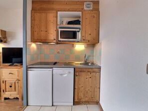A compact kitchen with wooden cabinets, a microwave, a dishwasher, and a tiled backsplash.