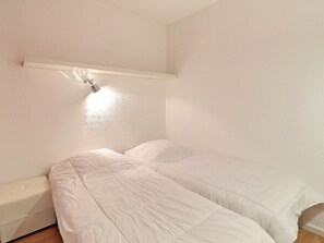 A bedroom with two beds, a bedside table, and a wall-mounted light fixture. - Comfortable 2-Room Ski-In Apartment, Pets Welcome (La Tania)