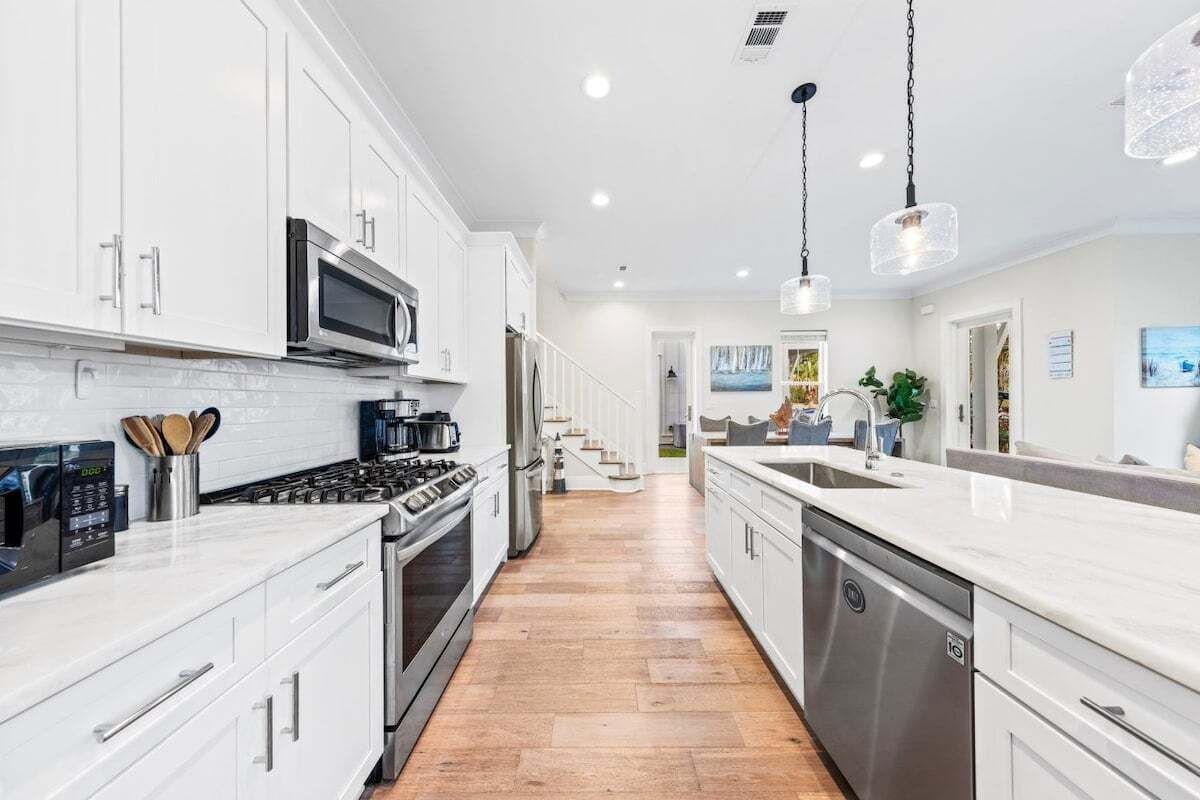 A modern kitchen with white cabinetry, stainless steel appliances, and a wooden floor.