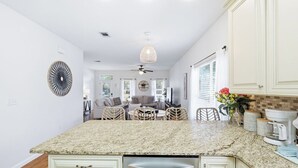 A kitchen with a granite countertop, white cabinets, a ceiling fan, and a dining area with wicker chairs. - Florida Cottage | Fenced yard| Serentiy Cottage | Hot Tub | Santa Rosa Beach (Santa Rosa Beach)