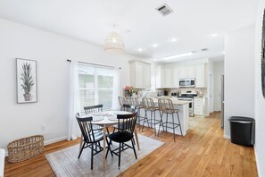 A modern kitchen with white cabinets, a dining area with a round table and chairs, and a visible trash bin.