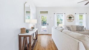 A living room with a sofa, a console table, a mirror, and a door leading outside. - Florida Cottage | Fenced yard| Serentiy Cottage | Hot Tub | Santa Rosa Beach (Santa Rosa Beach)