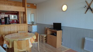 Ein gemütliches Zimmer mit Holztisch, einer Couch, einem Fernsehschrank und einer Küchenzeile mit einer Mikrowelle.