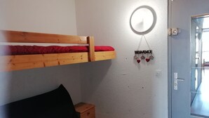 Ein Zimmer mit einem Etagenbett, einem kleinen Nachttisch, einer Tür und einer an der Wand befestigten Lampe.