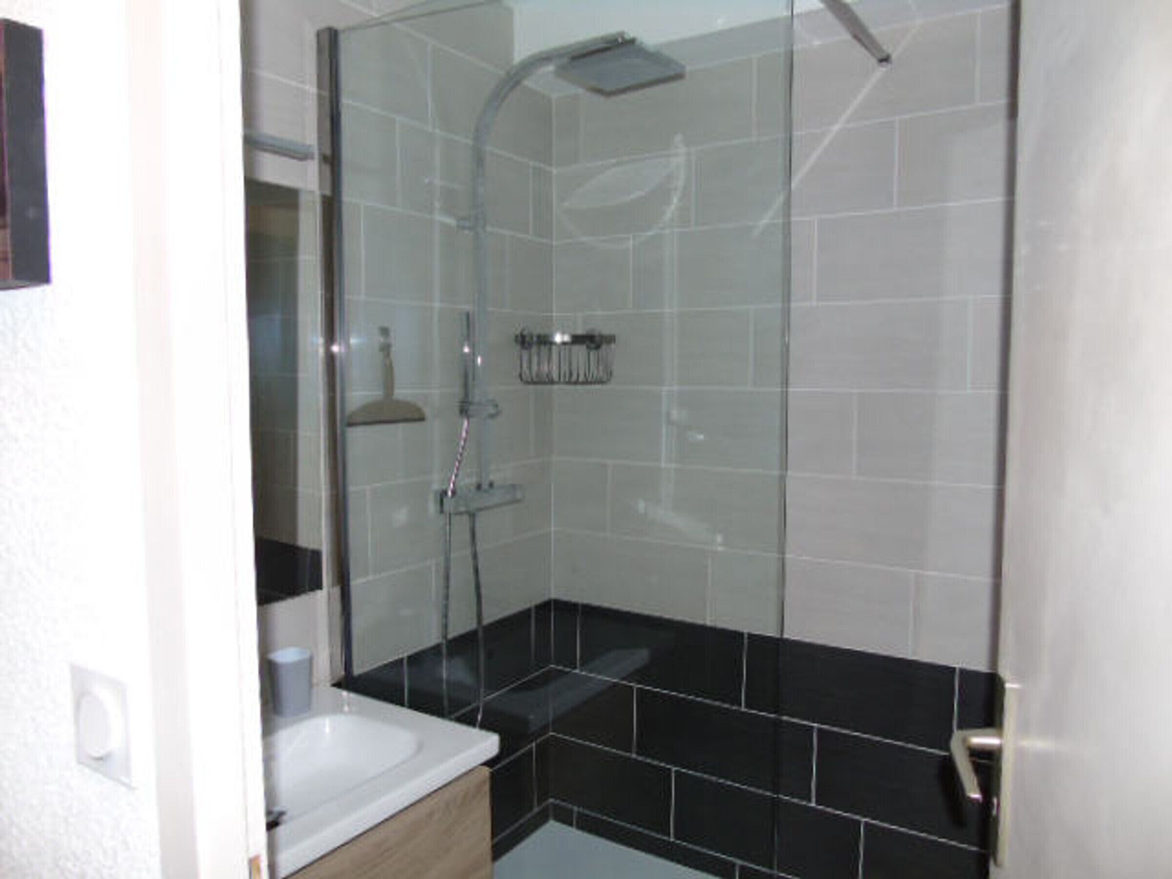 A modern bathroom with a glass-enclosed shower, a white sink, and black tiled flooring.